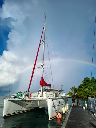 Whatabout Yacht Photos Pics 2005 Antares PDQ 44 catamaran docked under a rainbow, with lush greenery in the background.
