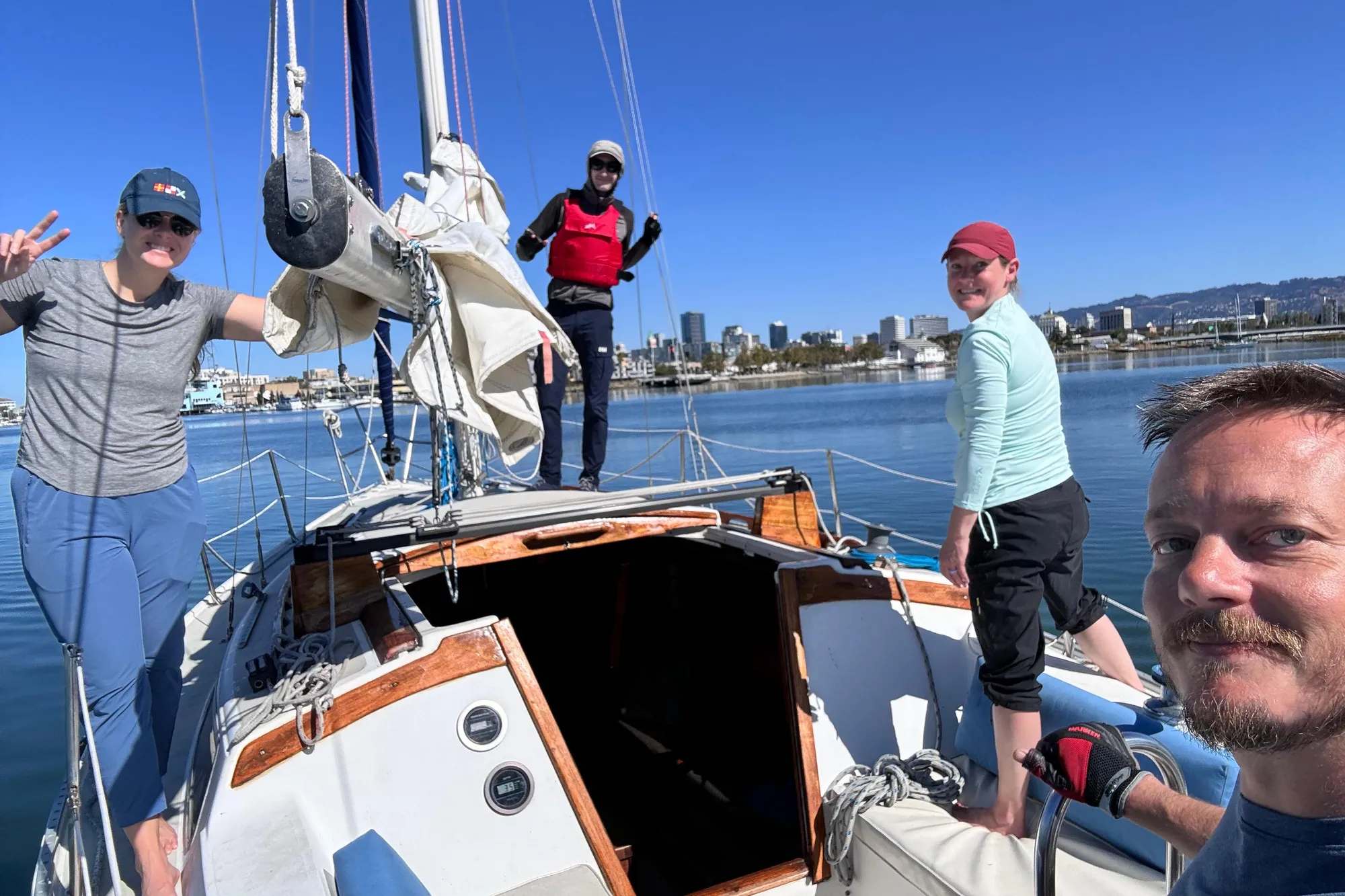 Group enjoying a sunny day on a 1980 Catalina 30 sailboat, with city skyline in background.