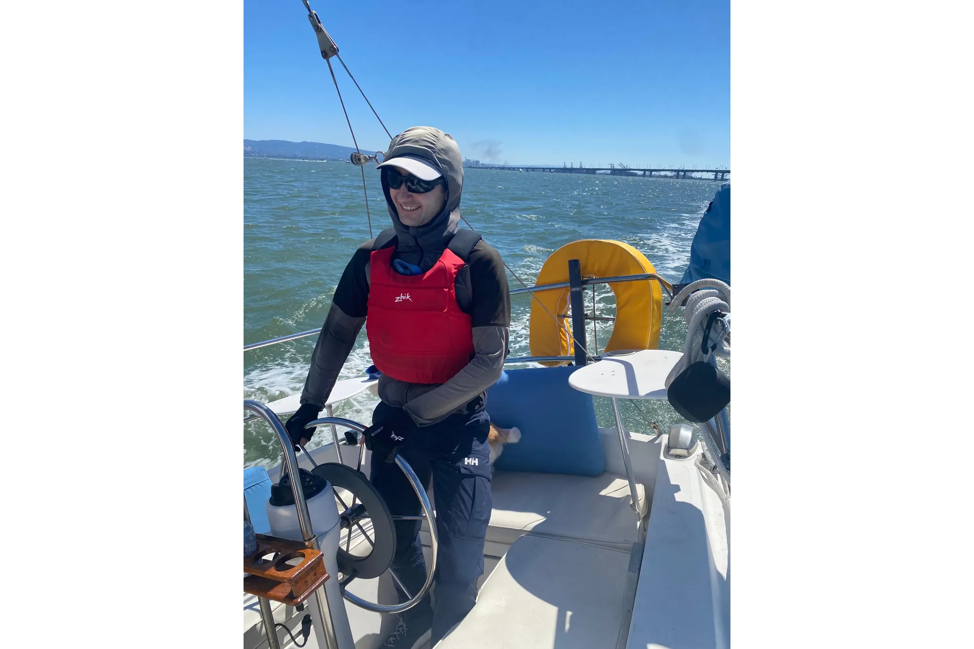 Person sailing a 1980 Catalina 30 boat on a sunny day, wearing a red life jacket.