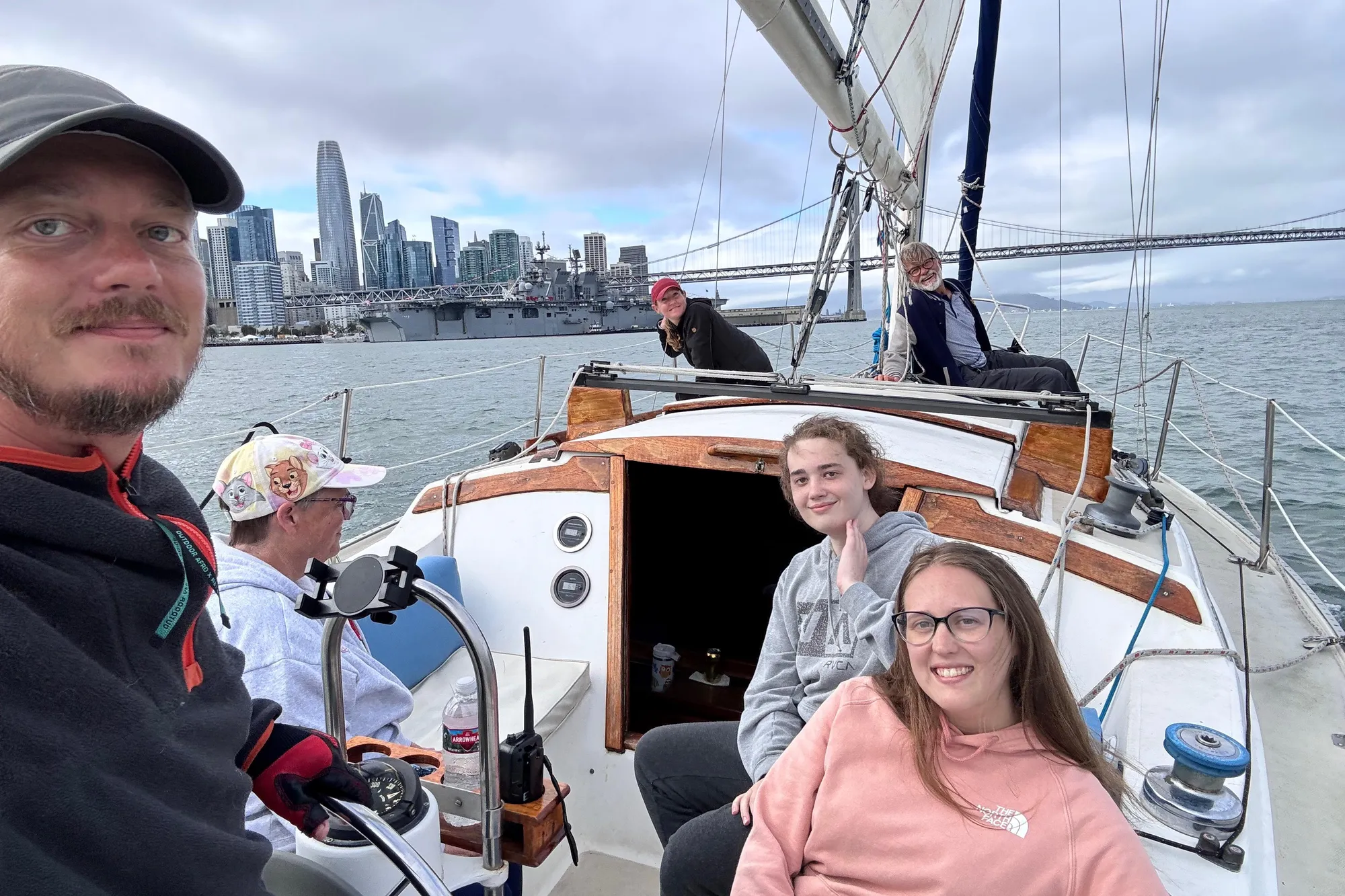 Group sailing on 1980 Catalina 30 yacht with city skyline and bridge in background.
