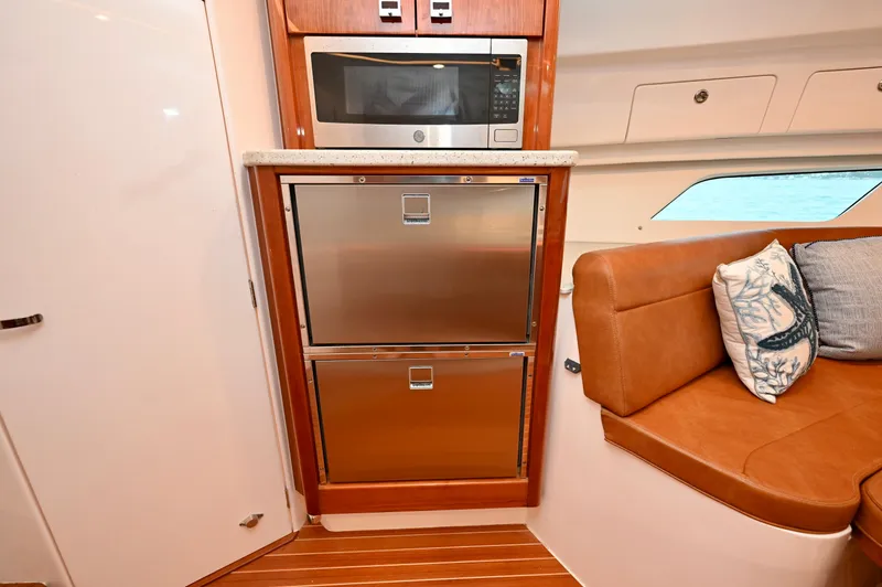  Yacht Photos Pics 2021 Intrepid 438 Evolution yacht interior with microwave, stainless steel drawers, and cushioned seating.