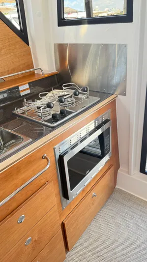  Yacht Photos Pics 2026 Cutwater C-288 Coupe interior kitchen with stove, microwave, and wooden cabinetry.