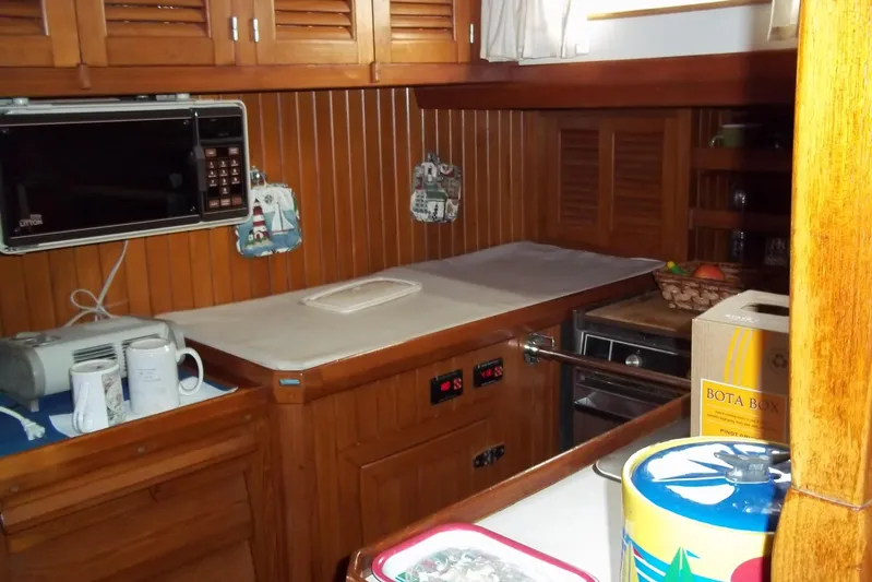 Trouvaille Yacht Photos Pics Wood-paneled galley kitchen in 1984 Slocum 43 sailboat with microwave and storage cabinets.