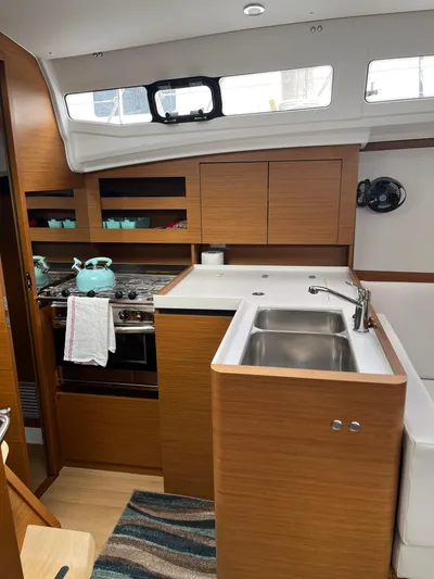 Resfeber Yacht Photos Pics Modern kitchen interior of 2023 Jeanneau Sun Odyssey 380 yacht, featuring wood cabinetry and stainless steel sink.