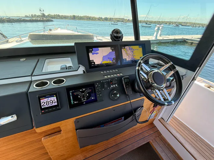Essi Yacht Photos Pics 2019 Axopar 37 Cabin helm with navigation screens and steering wheel, docked by the water.