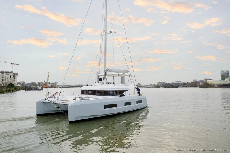  Yacht Photos Pics 2023 Lagoon 55 catamaran sailing on a calm river under a cloudy sky.