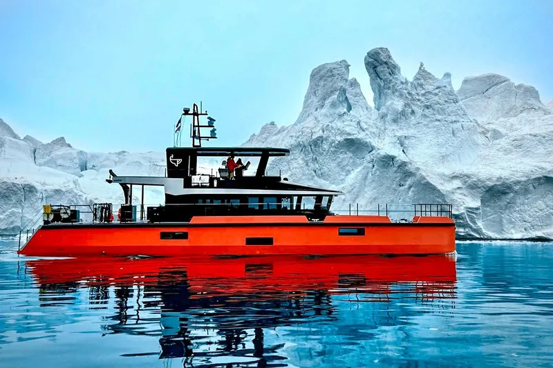 Vanguard Yacht Photos Pics 2023 Naval Yachts XPM 78 in icy waters, vibrant orange hull, majestic iceberg backdrop.