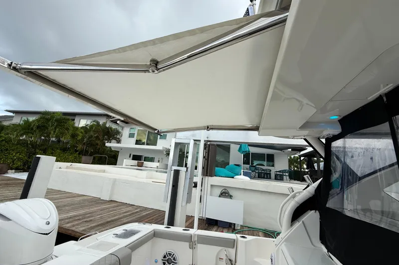 Yacht Photos Pics 2025 Pursuit OS 325 Offshore boat with extended canopy, docked near modern waterfront home.