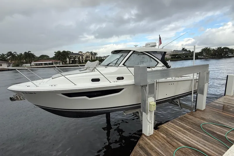 Yacht Photos Pics 2025 Pursuit OS 325 Offshore boat docked by waterfront homes under cloudy skies.