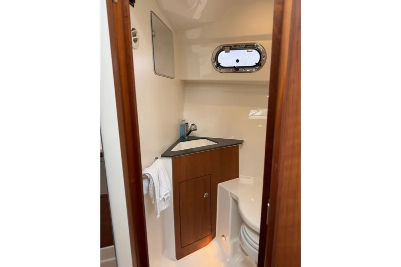  Yacht Photos Pics 2025 Pursuit OS 325 Offshore boat bathroom with wooden cabinetry and porthole window.