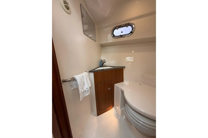  Yacht Photos Pics 2025 Pursuit OS 325 Offshore boat bathroom with sink, toilet, and porthole window.