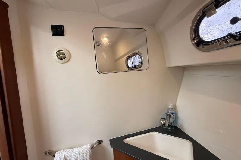  Yacht Photos Pics 2025 Pursuit OS 325 Offshore bathroom with sink, mirror, and porthole window.