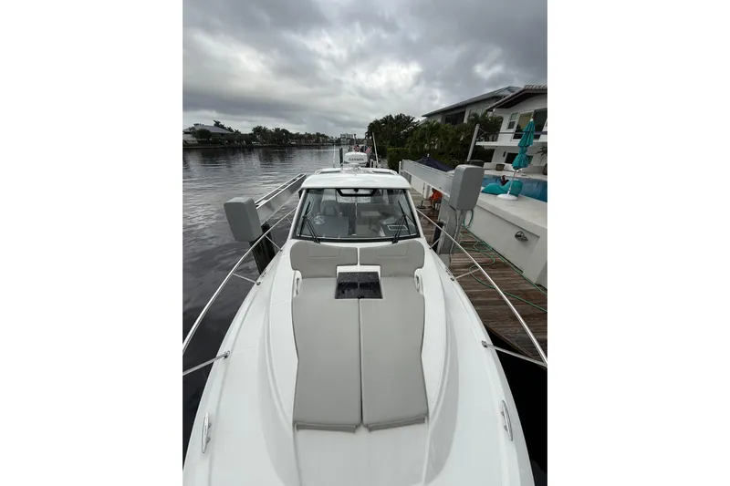  Yacht Photos Pics 2025 Pursuit OS 325 Offshore boat docked by a waterfront home under cloudy skies.