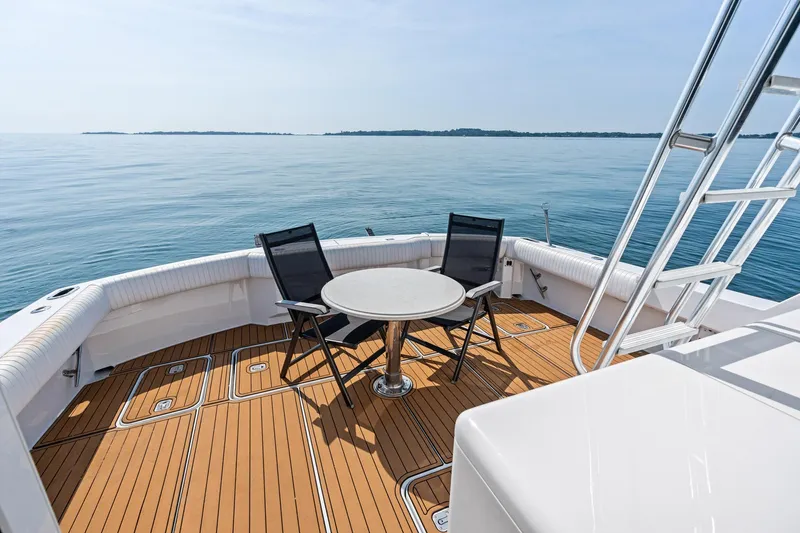 Amp'd Up Yacht Photos Pics 1999 Hatteras 60 Convertible yacht deck with chairs and table, overlooking calm sea.