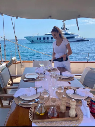Iduna Yacht Photos Pics Woman serving wine on 1939 Feadship Classic Sailing Yacht, with luxury yacht in background.