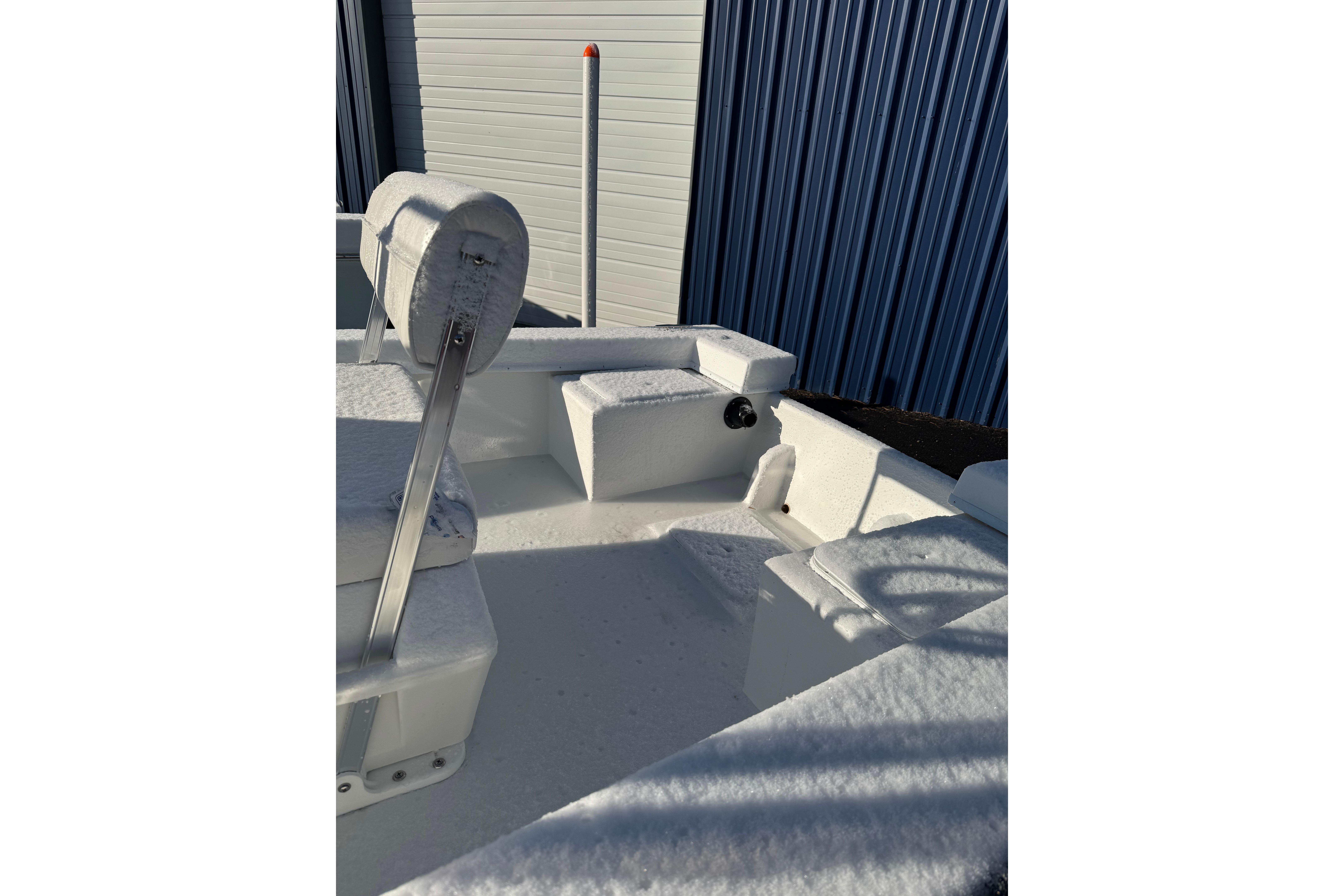 2026 C-Hawk 18 Center Console boat covered in snow, parked near a blue metal building.