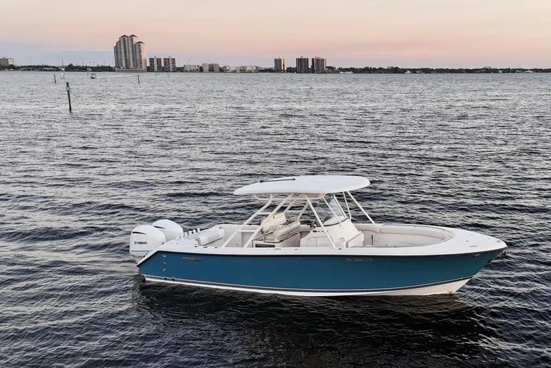  Yacht Photos Pics 2014 Pursuit S 280 Sport boat on calm water at sunset, city skyline in background.