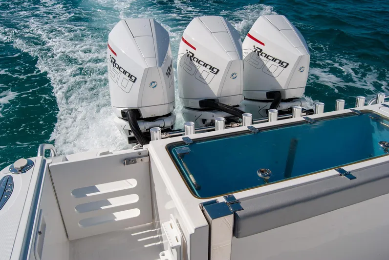  Yacht Photos Pics Triple outboard motors on a boat, cruising through blue ocean waters.