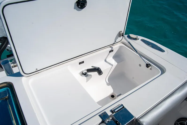  Yacht Photos Pics Open boat storage compartment with white interior, featuring a faucet and drain, against blue water background.