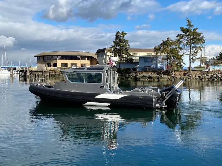  Yacht Photos Pics 2021 Life Proof 25 Full Cabin boat on calm water, with buildings and trees in the background.