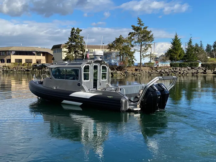  Yacht Photos Pics 2021 Life Proof 25 Full Cabin boat on calm water, with trees and buildings in the background.