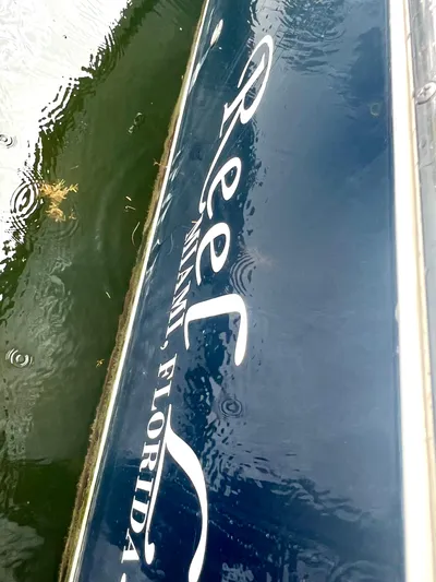 Reel Life Yacht Photos Pics Blue boat with "Reel Miami, Florida" text, water reflections, Jupiter 41SB, 2015 model.