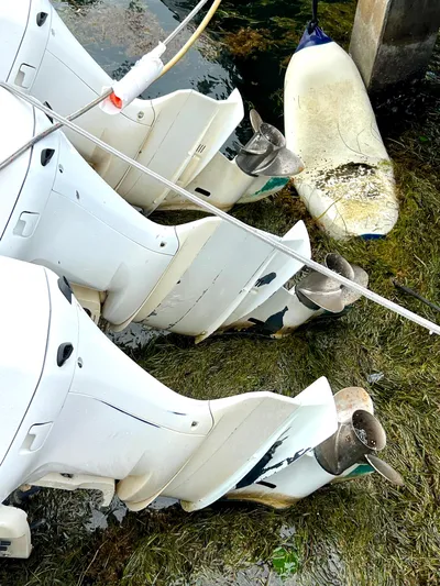 Reel Life Yacht Photos Pics Three outboard motors submerged in water near a dock, with a floating buoy nearby.