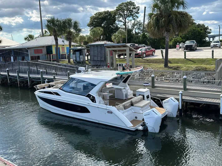  Yacht Photos Pics Aquila 36 Sport 2025 docked by a wooden pier with palm trees nearby.
