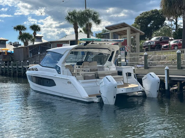  Yacht Photos Pics 2025 Aquila 36 Sport boat docked by a wooden pier under a partly cloudy sky.