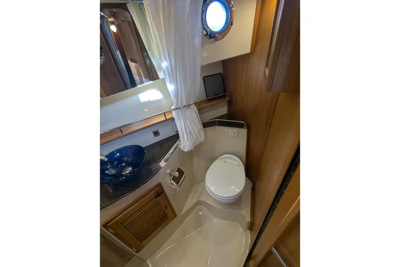 Lone Star Yacht Photos Pics 2022 Ranger Tugs R-31 S bathroom with porthole, blue sink, and wooden cabinetry.