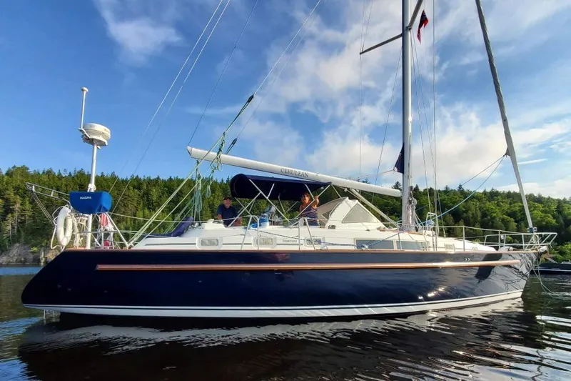  Yacht Photos Pics 1995 Beneteau Oceanis 44 CC sailboat on calm water, surrounded by lush greenery.