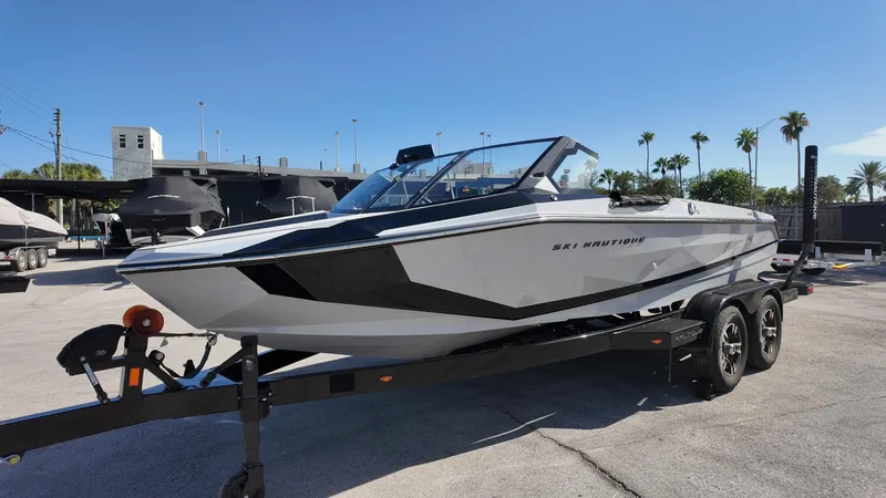  Yacht Photos Pics 2026 Nautique Ski boat on trailer, parked outdoors under clear blue sky.