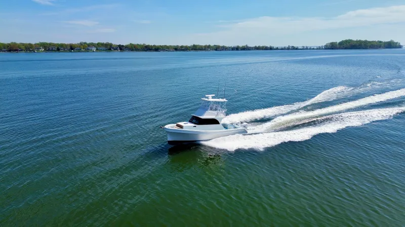Reel Conversation Yacht Photos Pics 2023 Millennium Marine NuWave 37 cruising on a serene lake under a clear blue sky.
