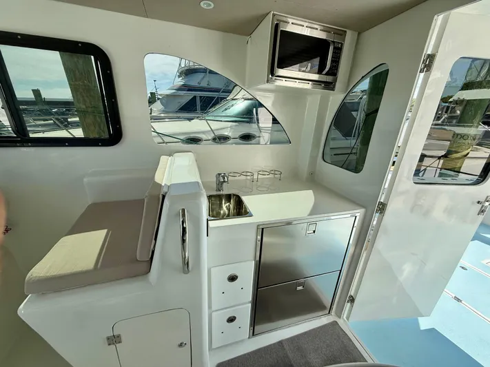 Reel Conversation Yacht Photos Pics Interior of 2023 Millennium Marine NuWave 37, featuring kitchenette with sink, microwave, and seating.