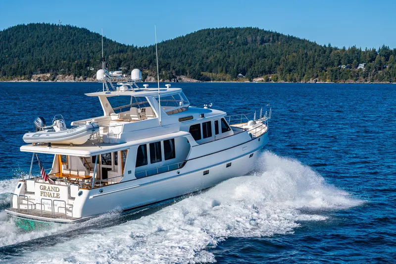 Grand Finale Yacht Photos Pics 2007 Grand Banks 59 Aleutian yacht cruising on blue waters near forested shoreline.