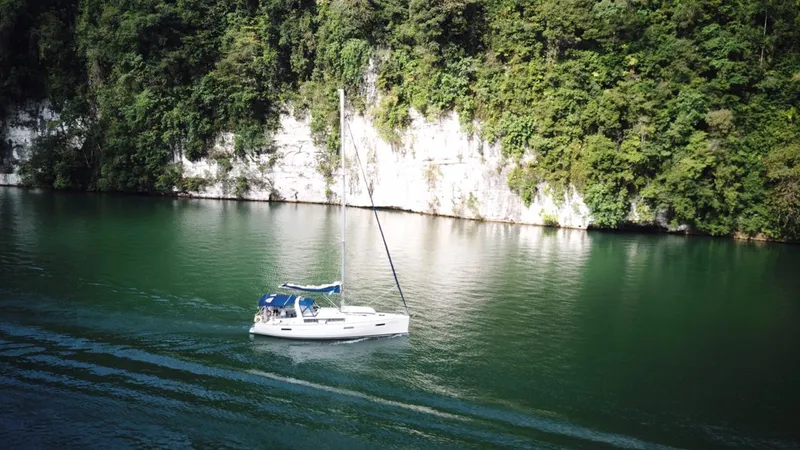 Sv Tonic III Yacht Photos Pics Sailboat Beneteau Oceanis 41.1 (2012) cruising on a serene, green river with lush cliffs.