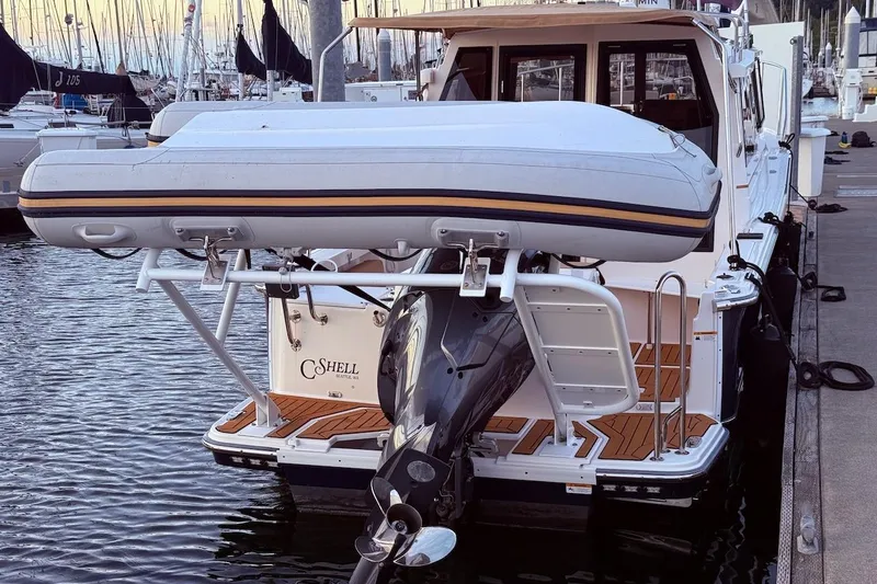 C Shell Yacht Photos Pics 2022 Ranger Tugs R-27 with dinghy, docked at marina, showcasing rear view and motor.