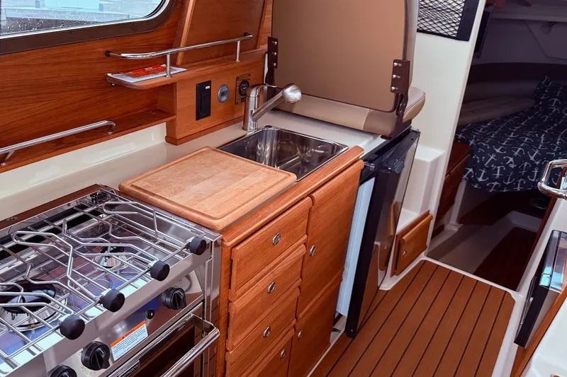 C Shell Yacht Photos Pics 2022 Ranger Tugs R-27 interior kitchen with stove, sink, and wooden cabinetry.