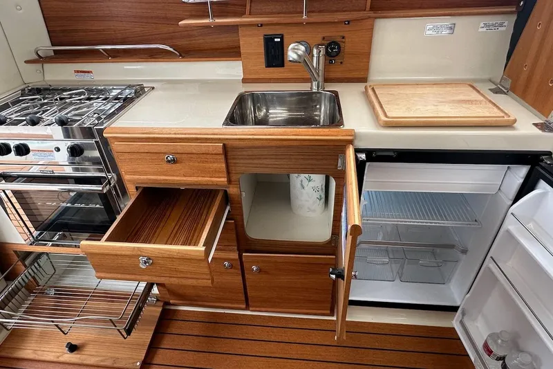 C Shell Yacht Photos Pics 2022 Ranger Tugs R-27 galley with stove, sink, fridge, and wooden cabinetry.