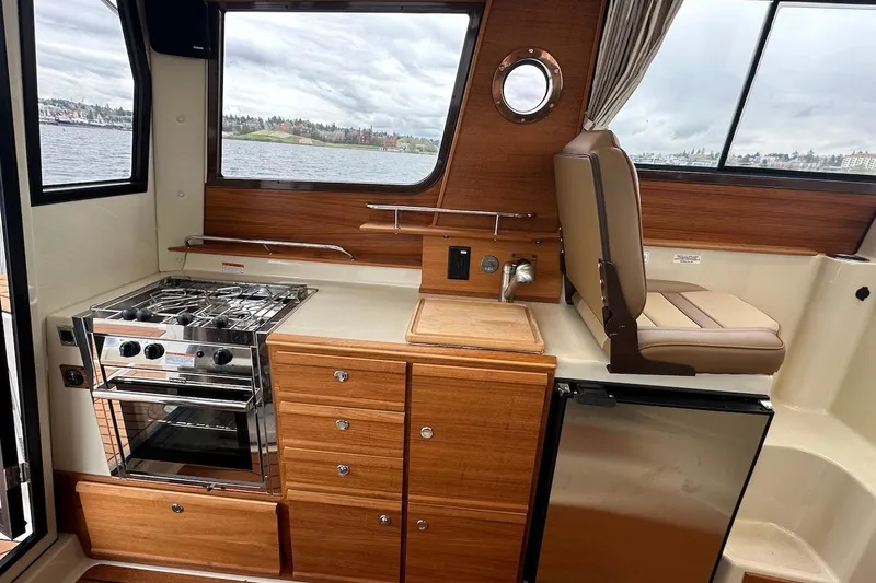 C Shell Yacht Photos Pics Interior of 2022 Ranger Tugs R-27 with kitchen and seating area, featuring wood cabinetry.
