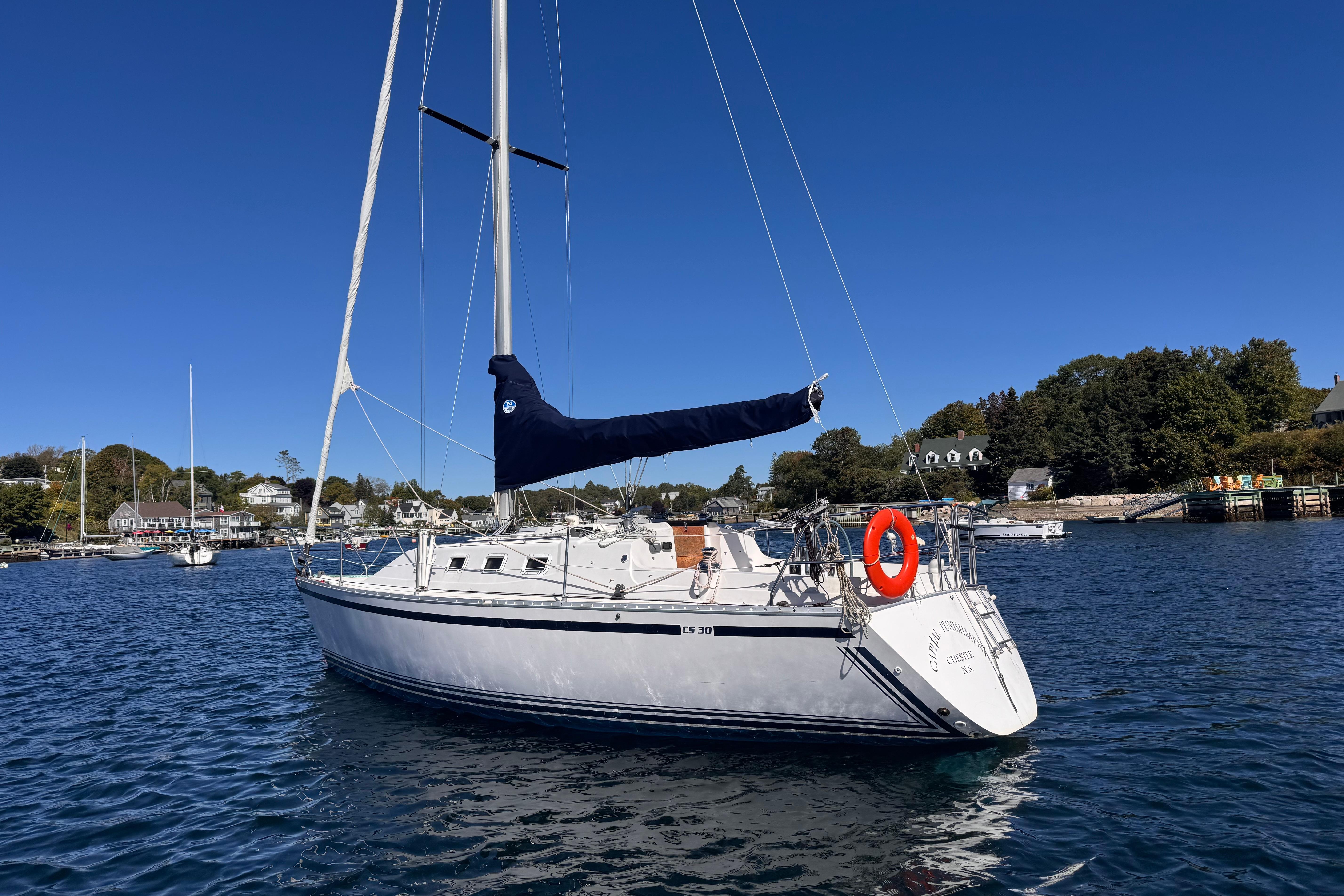 1986 CS 30 sailboat anchored in a scenic harbor under a clear blue sky.