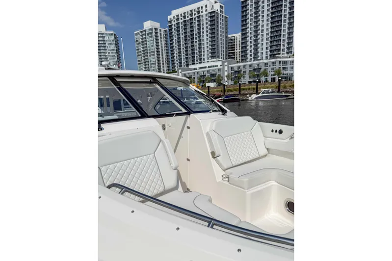  Yacht Photos Pics 2024 Pursuit DC 365 Dual Console boat with luxurious seating, docked near modern high-rise buildings.