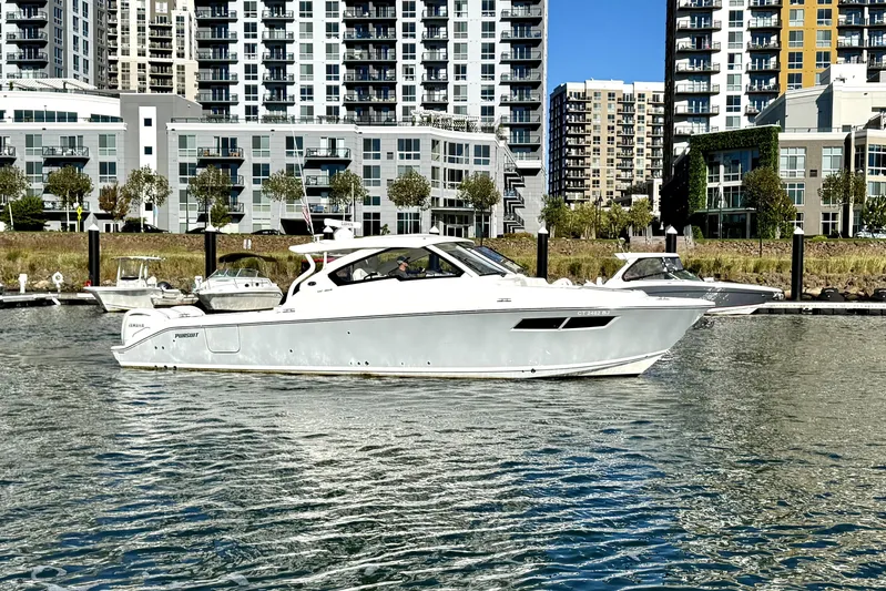  Yacht Photos Pics 2024 Pursuit DC 365 Dual Console boat on water with cityscape background.