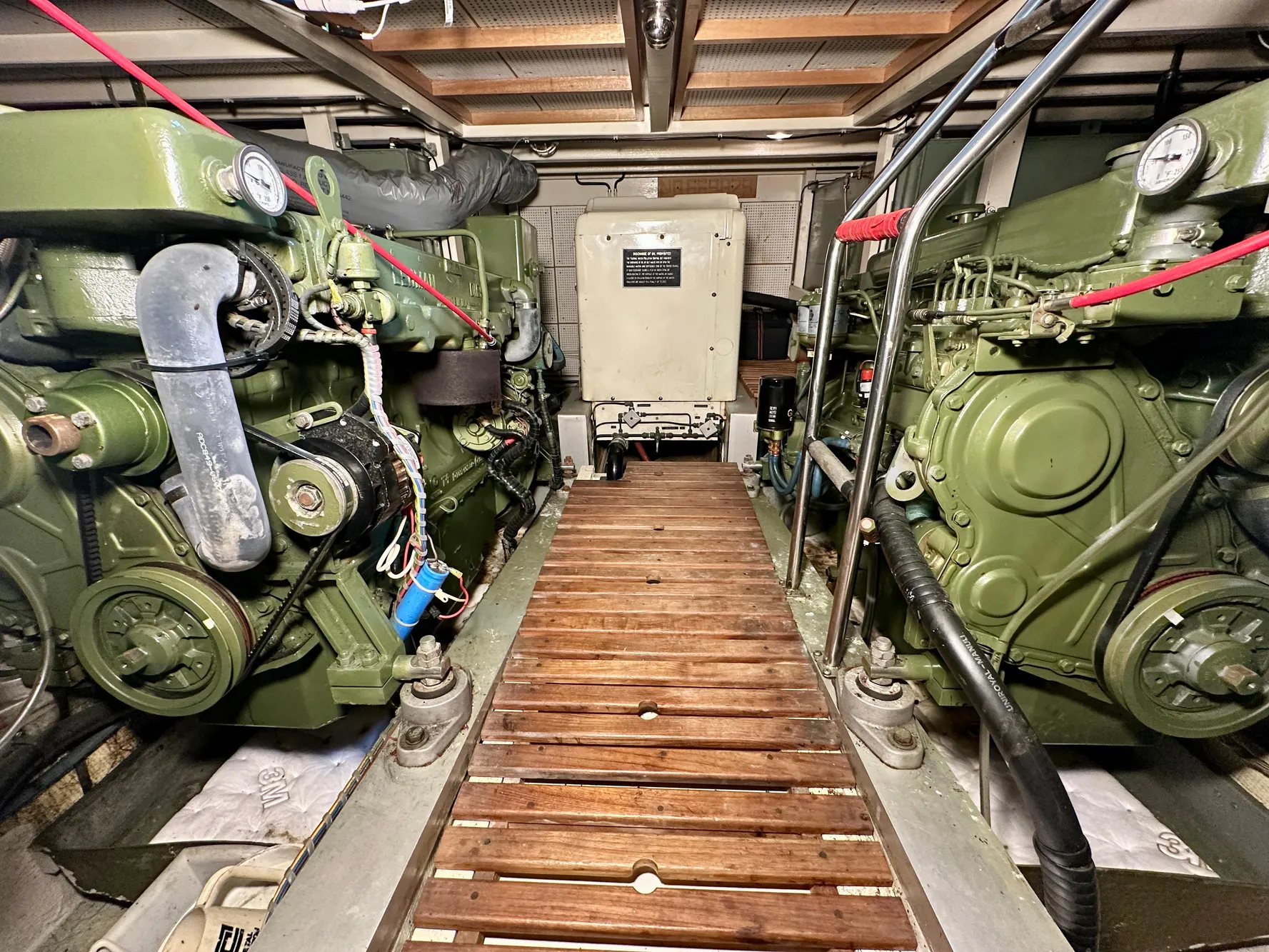 Engine room of 1982 Grand Banks Classic boat with dual green engines and wooden walkway.