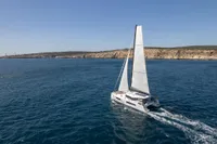 Sailing catamaran Nautitech 44 Open 2026 cruising on open sea near rocky coastline.