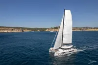 Sailing catamaran Nautitech 44 Open 2026 gliding on blue ocean near rocky coastline.