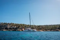 2026 Nautitech 44 Open catamaran sailing near a rocky coastline under a clear blue sky.