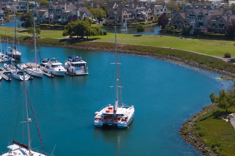 In Stock Yacht Photos Pics 2024 Excess 14 catamaran docked in a serene marina with waterfront homes.