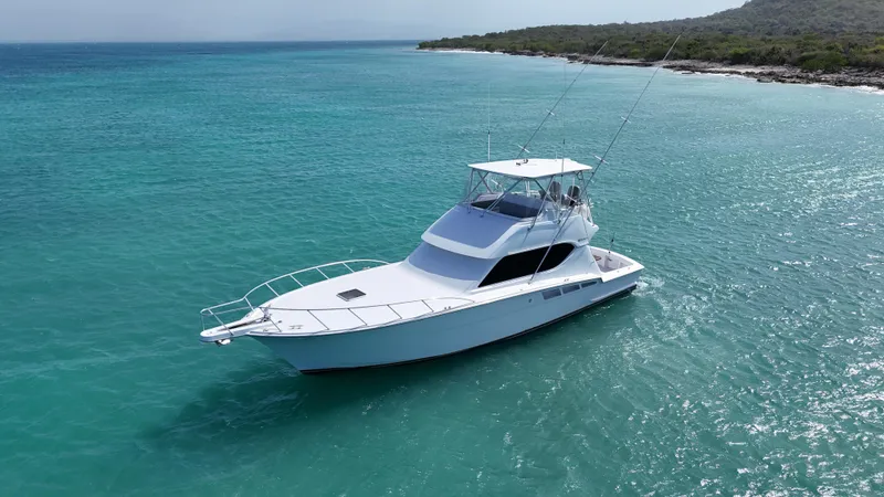  Yacht Photos Pics 2005 Hatteras 50 Convertible yacht cruising in clear turquoise waters near a scenic coastline.