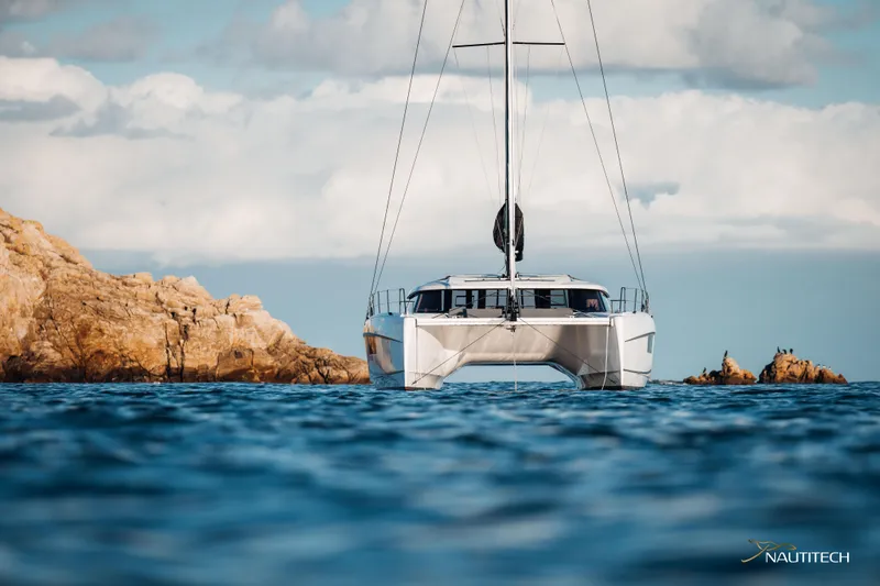 Nautitech 48 Open - Available For 2026 Delivery! Yacht Photos Pics Front view of Nautitech 48 Open (2025) catamaran sailing near rocky coastline.
